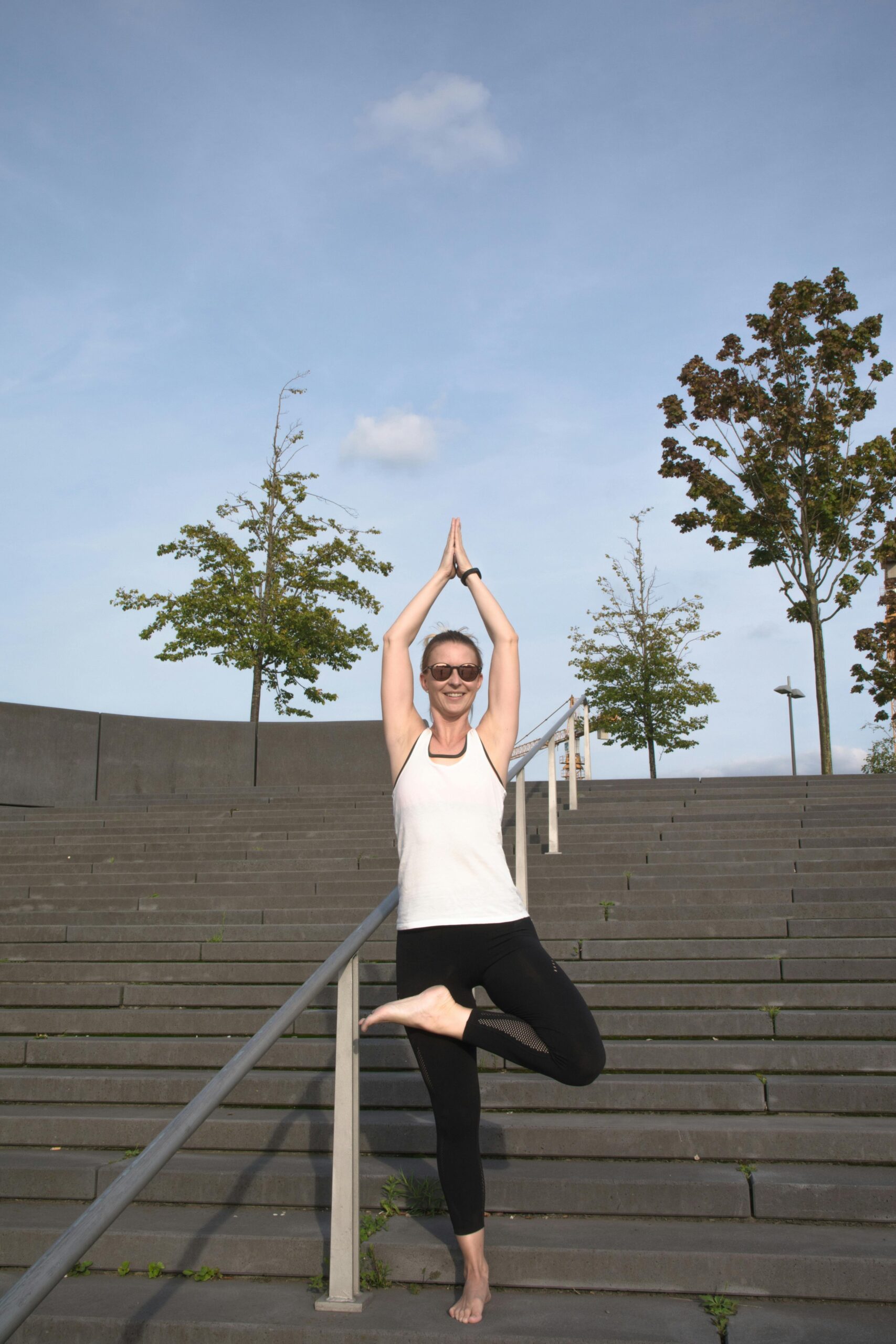 Woman practicing yoga tree pose on urban stairs in Bremen, Germany on a sunny day.