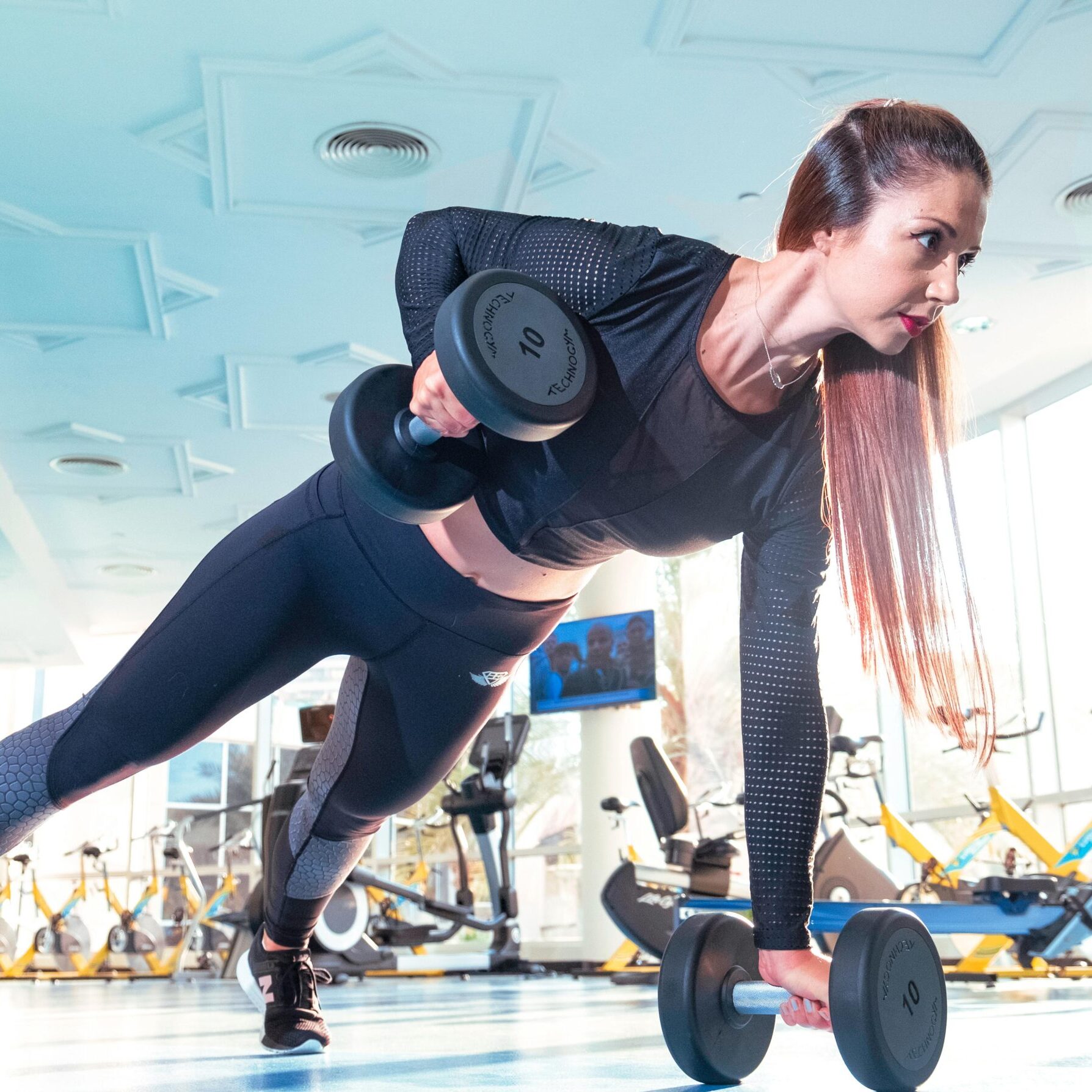 Woman performing a plank row with dumbbells in a bright Dubai gym.