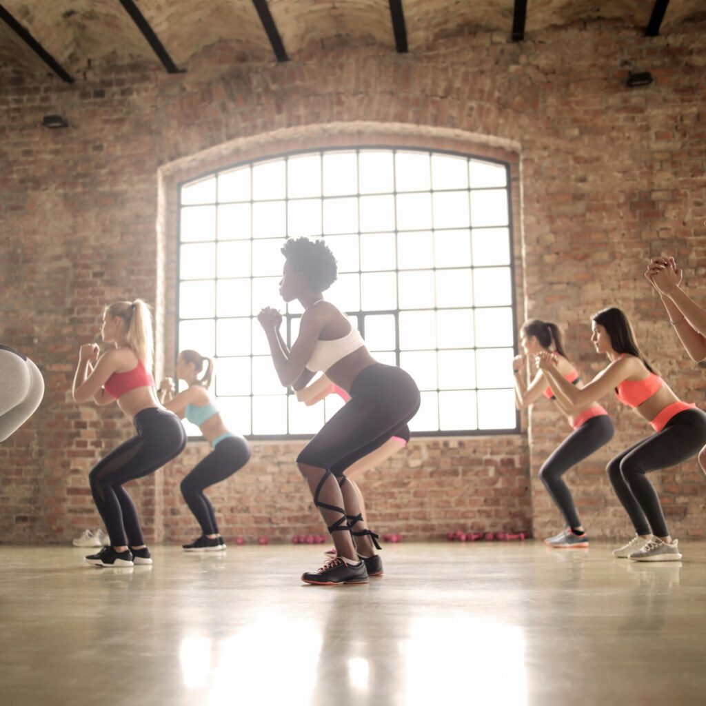 Women participating in a group fitness class performing squats in an industrial-style studio.