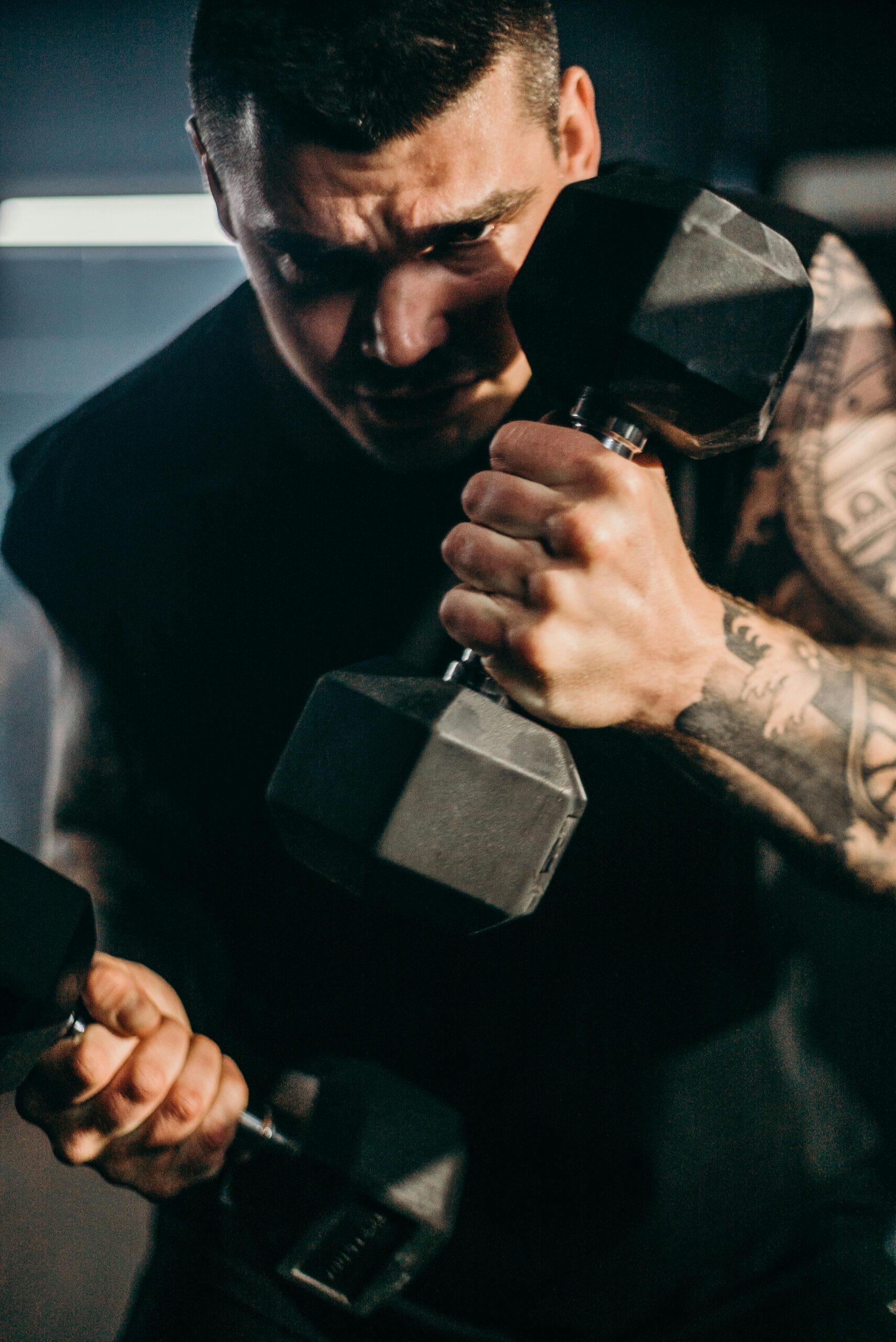 Focused athlete lifting dumbbells in gym, showcasing strength and tattoos.